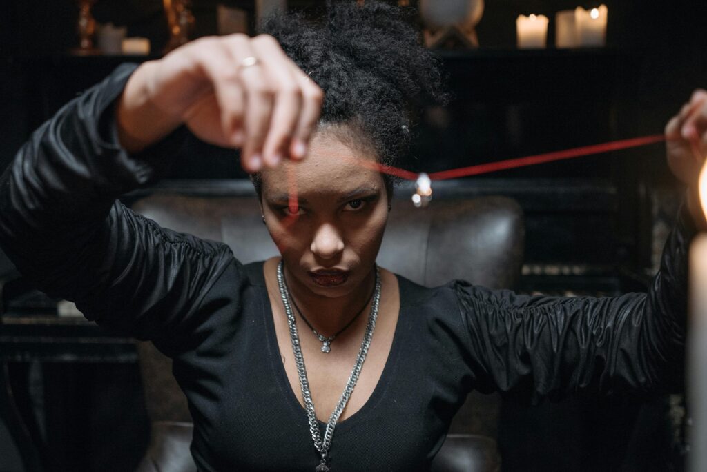 A young woman in a mysterious setting, holding a pendant with intense gaze and dim candlelight.