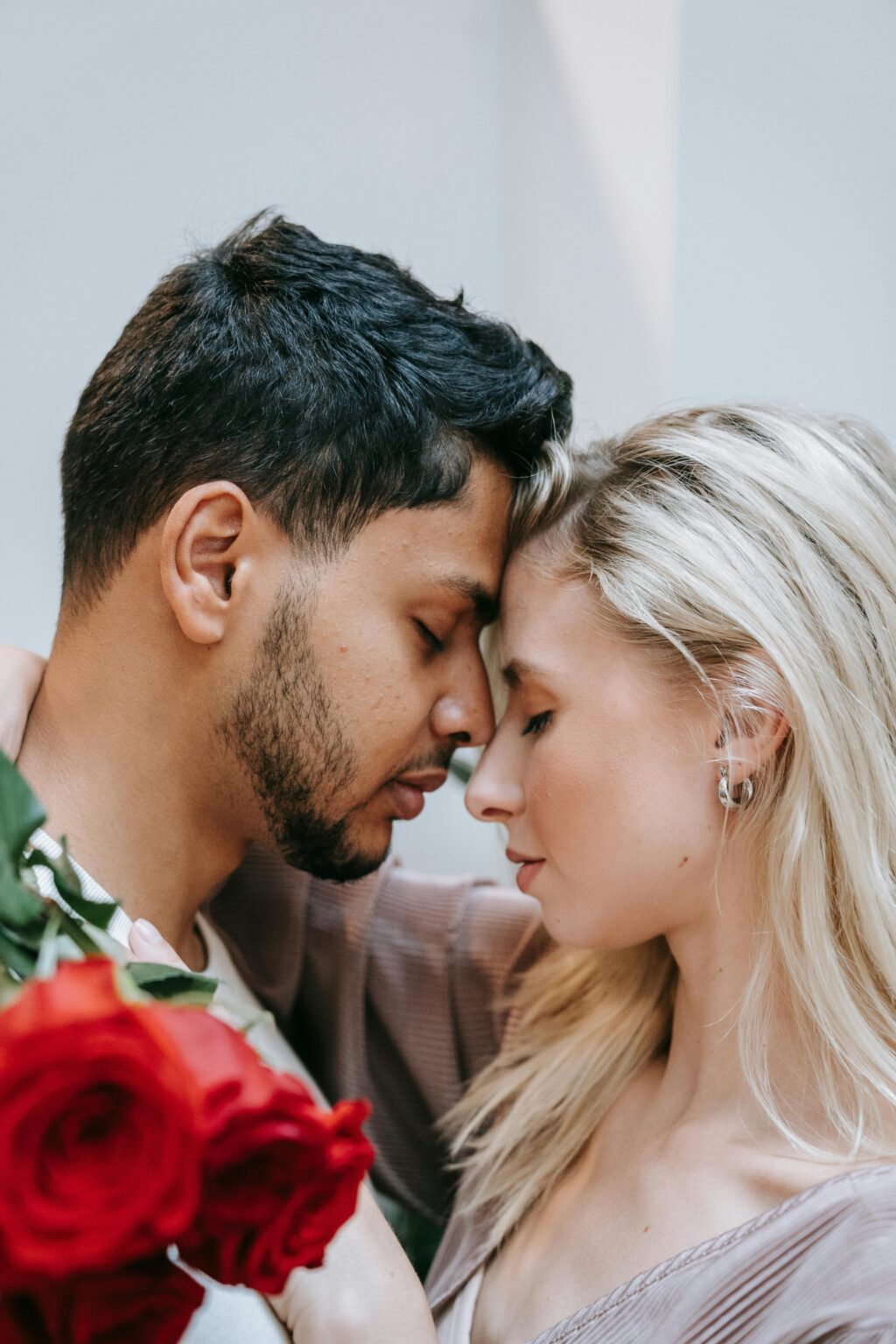 Tender moment between an interracial couple indoors with roses, symbolizing love and affection.
